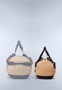 Des sacs de voyage ronds en beige et tan, dotés d'accents noirs, de poignées doubles et de sangles ajustables. Tissu doux avec une texture lisse.