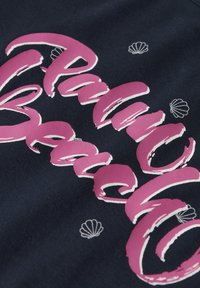 Tela azul marino con letras rosas llamativas que dicen "Palm Beach" con detalles en blanco. Pequeños motivos de conchas dispersos alrededor del texto. Apariencia texturizada.