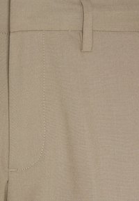 Beige Hosen aus strukturiertem Stoff, mit flachem Bund, sichtbaren Nähten und detaillierten Seitentaschen.