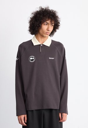 Mörkgrå långärmad polo med en ljusbeige krage, prydd med broderad logotyp på bröstet och vänster ärm, tillverkad av mjukt bomullsmaterial.