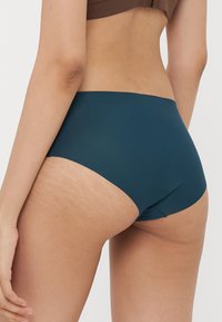 Cuecas altas em teal com uma textura suave e costuras mínimas, exibindo uma vista sutil da parte superior das costas e um contraste na textura da pele.