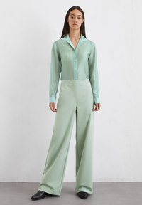 Lichtgroene overhem shirt met een kraag en lange mouwen, gecombineerd met wijde groene broek. Gladde stofstructuur en eenvoudig ontwerp.