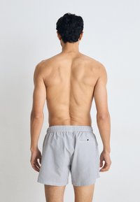 Calções de banho risca em cinza claro com cintura ajustável por cordão e bolso traseiro. Feitos de tecido leve e liso, desenhados para conforto.