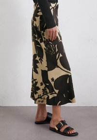 Czarna spódnica midi w kwiatowy wzór na beżowym tle, charakteryzująca się gładką fakturą materiału i sylwetką A-linii. Stylizowana z czarnymi sandałami.