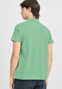 Zelená polo tričko s krátkým rukávem, hladkým povrchem, límečkem a rovním lemem. Jednoduchý, moderní design, vhodný na běžné nošení.
