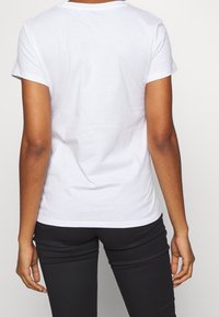 Biały bawełniany T-shirt z krótkimi rękawami, okrągłym dekoltem i gładkim tyłem. Połączony z czarnymi dopasowanymi spodniami, podkreślając prosty design.