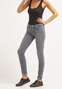 Jeans skinny grises de denim, con un diseño clásico de cinco bolsillos y un ligero desgastado, combinados con zapatillas negras de corte bajo.