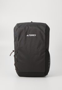 Black Terrex backpack with a smooth fabric surface, rounded shape, front zip pocket, side mesh pocket, and decorative cord detailing.