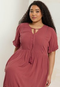 Valkoisella hameella, jossa on lyhyet, röyhelöiset hihat, avainreikään kuuluva kaula-aukko, nappi yksityiskohta ja kerätty vyötärö, jossa on tupsu koristelut.