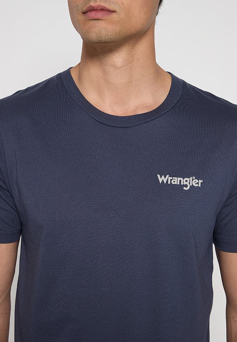 T-shirt blu scuro in cotone morbido, con scollatura rotonda e maniche corte. Logo "Wrangler" in bianco, posizionato sul lato sinistro del petto.
