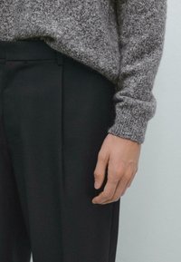 Pull en maille gris avec un tissu texturé, coupe décontractée. Assorti à un pantalon noir ajusté, avec une finition lisse et un design structuré.