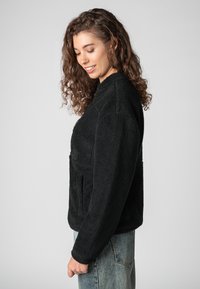 Schwarze Fleecejacke mit strukturierter, weicher Außenseite, ausgestattet mit hohem Kragen und Fronttaschen, kombiniert mit hellblauer Denim.