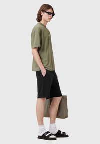 Olive green oversized t-shirt with short sleeves, paired with black shorts. Accessories include black sunglasses and black sandals with straps.