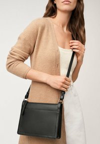 Sacoche en cuir noir en forme rectangulaire, avec fermeture éclaire et bandoulière réglable. Texture lisse avec des accents de quincaillerie minimalistes.