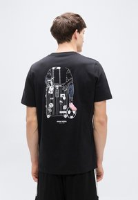 Μαύρο βαμβακερό t-shirt με γραφικό σχέδιο αποσκευή, χέρια και ποδοσφαιρική μπάλα στην πλάτη. Λεπτομέρειες με πολύχρωμες πινελιές και μοτίβα.