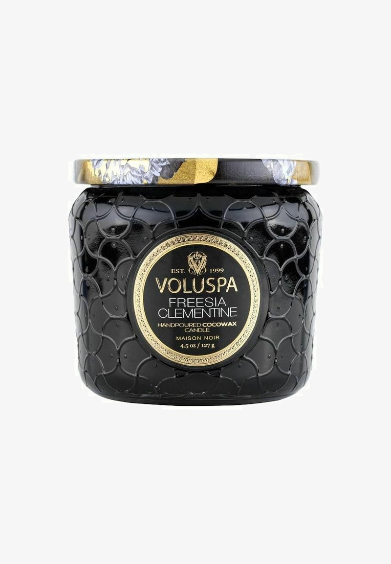 Svart, texturerad ljusbehållare med ett lock som har gulddetaljer. Etiketten visar "Voluspa Freesia Clementine", 4,5 oz, handgjord cocowax.