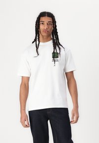 Hvit bomulls T-skjorte med kort erm, med en grønn grafisk design på venstre bryst og teksten "the new originals" under.