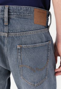 Blauwe denim jeans met een leren label aan de achterkant. Kenmerken zijn onder andere een klassiek vijfzakendesign en oranje stiksels langs de naden.