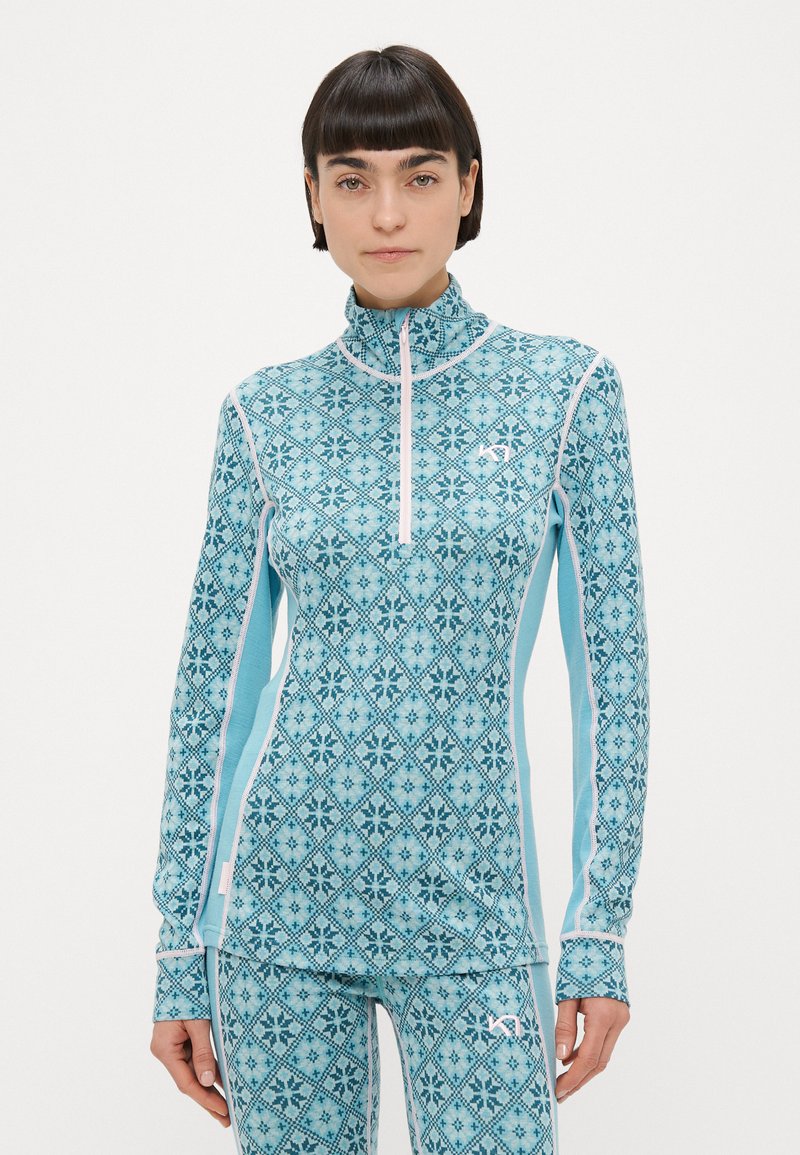 Αθλητική μπλούζα ανοιχτού γαλάζιου με ψηλό γιακά και διακοσμητικό μοτίβο σε σχήμα διαμαντιού. Διαθέτει μακριά μανίκια και λευκές λεπτομέρειες κατά μήκος των ραφών.