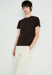 Brown cotton t-shirt with short sleeves, crew neck, and subtle texture, paired with light beige relaxed-fit trousers.