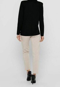 Černý top s dlouhým rukávem a rovný střih, spárovaný se světle béžovými slim-fit kalhotami a černými kotníkovými botami s jemným designem.