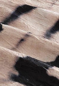 Tissu beige froissé avec des formes noires abstraites et irrégulières et des ombres douces mettant en valeur la texture et les plis.