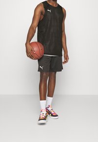 Canotta nera, pantaloni corti neri, sneakers colorate con motivo e un pallone da basket. L'insieme è sportivo e funzionale.