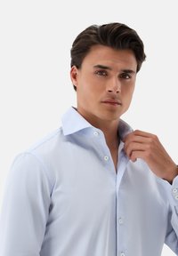 Helltürkises Hemdkleid mit spitzem Kragen, langen Ärmeln und kontrastierenden weißen Knöpfen. Glatte Textur, taillierte Passform.