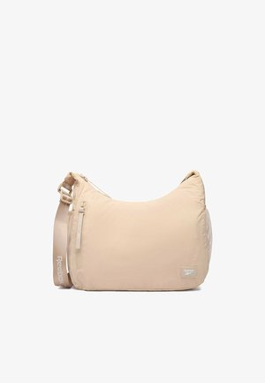 Beżowa torba na ramię Reebok z regulowanym paskiem, przednią kieszenią na zamek, boczną kieszenią z siateczki oraz naszywką z logo w prawym dolnym rogu.