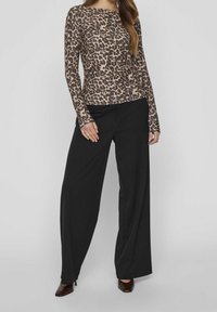 Långärmad topp med leopardmönster i brunt och beige, tillsammans med vida svarta byxor. Slät tygtextur, figursydd design.