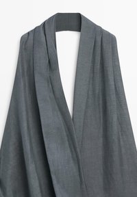 Col châle gris doux drapé sur un cintre avec un tissu texturé visible et des plis délicats.