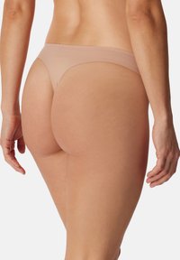 Nøgen sømløs trusse i thongs stil med et minimalistisk design, blød tekstur og let stræk samt en lav talje bagpå.