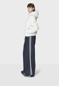 Hvid puffjakke med hætte, der har en firkantet lap. Båret sammen med marineblå vidde jeans, accentueret med grå sidelapper.