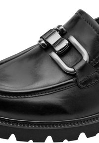 Mocassin en cuir noir avec boucle métallique argentée et semelle épaisse à profondes rainures, en gros plan.
