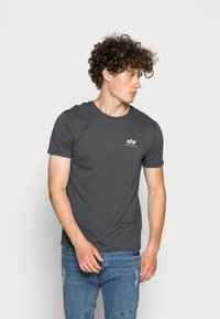 Graues T-Shirt mit kurzen Ärmeln aus einem glatten, baumwollähnlichen Stoff. Mit kleinem weißen Logo auf der linken Brust und klassischem Rundhalsausschnitt.