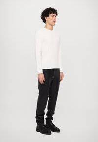 Hvid langærmet skjorte i struktureret stof, parret med sorte læderbukser med en synlig lynlås. Sorte støvler fuldender outfittet.