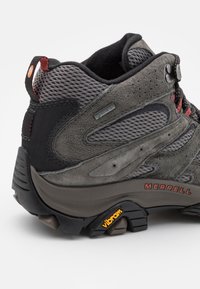 Szare buty trekkingowe z teksturowanej zamszowej i siateczkowej cholewki, z wzmocnionym piętą, czerwonymi akcentami oraz podeszwą Vibram dla lepszej przyczepności.