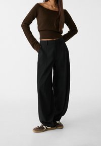 Pull marron court avec ourlet côtelé associé à un pantalon noir ample. Baskets marron arrondies avec lacets blancs et détails blancs.