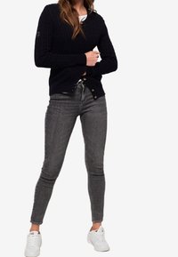 Marineblaue Strickjacke mit Rippdetails und Knopfverschluss, kombiniert mit grauen Slim-Fit-Jeans und weißen Sneakers und so ein lässiges Outfit kreierend.