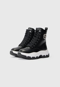 Adidași negri tip ghetă, cu tălpi groase de cauciuc alb, șireturi negre, logo Guess pe limbă și un emblema decorativă argintie pe lateral.