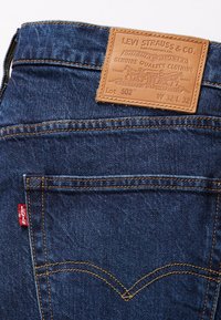 Poche arrière d'un jean en denim bleu avec couture orange, étiquette rouge Levi's et étiquette en cuir marron Levi Strauss & Co. indiquant la taille W32 L32, modèle 502.