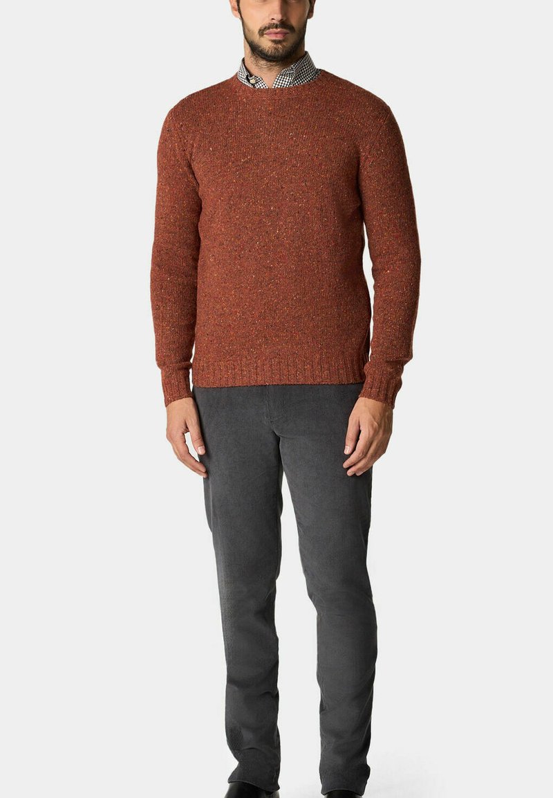 Oranžový pletený svetr s texturou a kulatým výstřihem, nošený přes kostkovanou košili, doplněný o šedé slim-fit kalhoty.