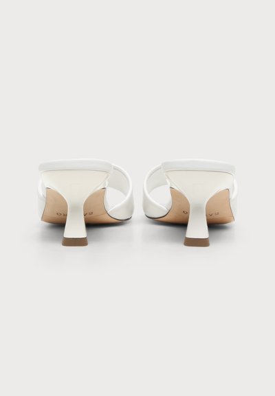 Paire de sandales blanches à talons ouverts vues de dos, avec des talons blocs bas et des larges brides à l'avant.