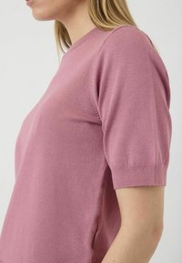 Pletena majica s kratkim rukavima u ružičastoj boji s okruglim izrezom i glatkom teksturom, sa ležernim krojem i rebrastim detaljima na rukavima.