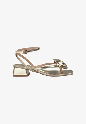 Goldfarbene metallische Sandalen mit Blockabsatz, ausgestattet mit gekreuzten Riemen und einem floralen Akzent an der Zehe. Glatte Textur, offenes Design.