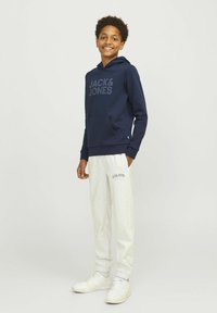 Modra kapuca s sprednjim logotipom "JACK & JONES", v kombinaciji s svetlo sivimi trenirkami z detajlom logotipa in belimi športnimi copati. Casual fit.