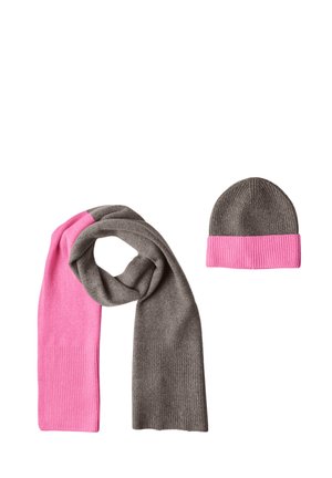 Écharpe en tricot gris et rose en boucle à côté d'un bonnet gris assorti avec un revers rose plié sur fond blanc.