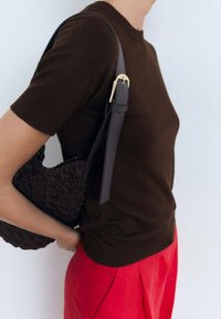 Pull court en tricot marron à manches courtes associé à un pantalon rouge taille haute. Un sac noir texturé pend d'une sangle foncée avec des garnitures dorées.