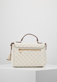 Borsa a mano color crema con un sottile motivo circolare, manico in pelle marrone, una tasca frontale con zip e un dettaglio in pelle a frange attaccato.