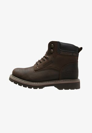 Brązowy skórzany but za kostkę z wytrzymałą podeszwą, okrągłym noskiem, metalowymi oczkami i wyściełanym kołnierzem. Posiada logo po boku.